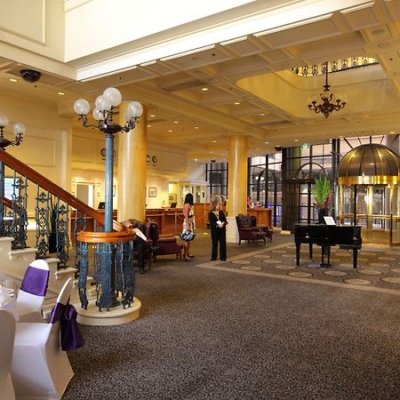 Stamford Grand Adelaide Hotel Glenelg Nội địa bức ảnh The photo shows a luxurious interior of a hotel or a restaurant lobby. There is an elegant staircase with ornate railings leading to an upper level. The space features high ceilings with decorative chandeliers and ample natural light coming through l
