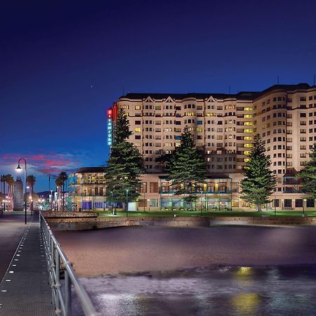 Stamford Grand Adelaide Hotel Glenelg Ngoại thất bức ảnh The photo shows a waterfront scene at dusk, featuring a large building lit up against a darkening sky. The architecture appears modern and prominent, with several windows illuminated. In the foreground, there is a walkway or pier with fencing along t