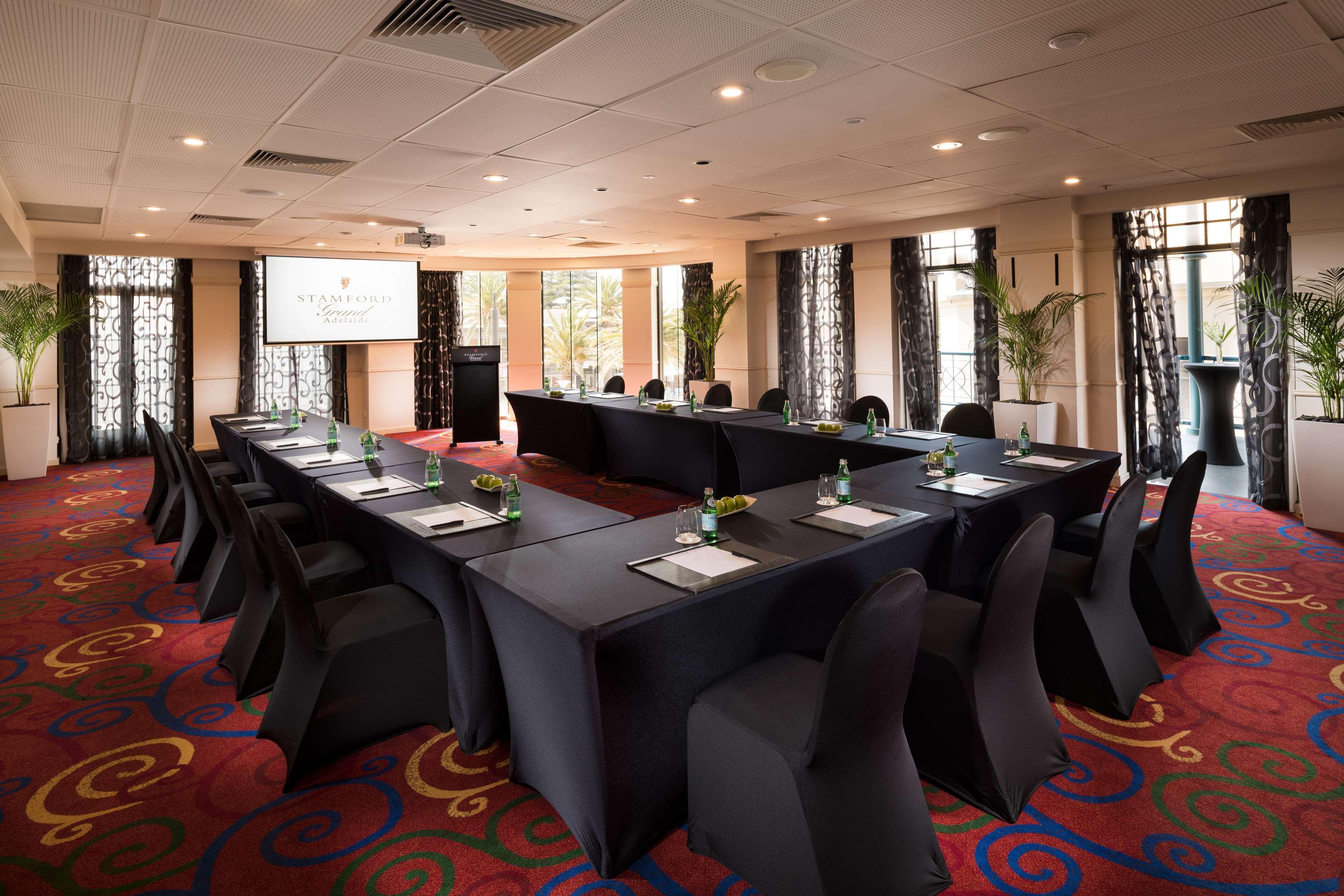 Stamford Grand Adelaide Hotel Glenelg Ngoại thất bức ảnh The photo shows a conference room set up for a meeting or presentation. There are several tables arranged in a U-shape, covered with black tablecloths. Each table has a notepad and a small bottle of water on it. The chairs around the tables are also 
