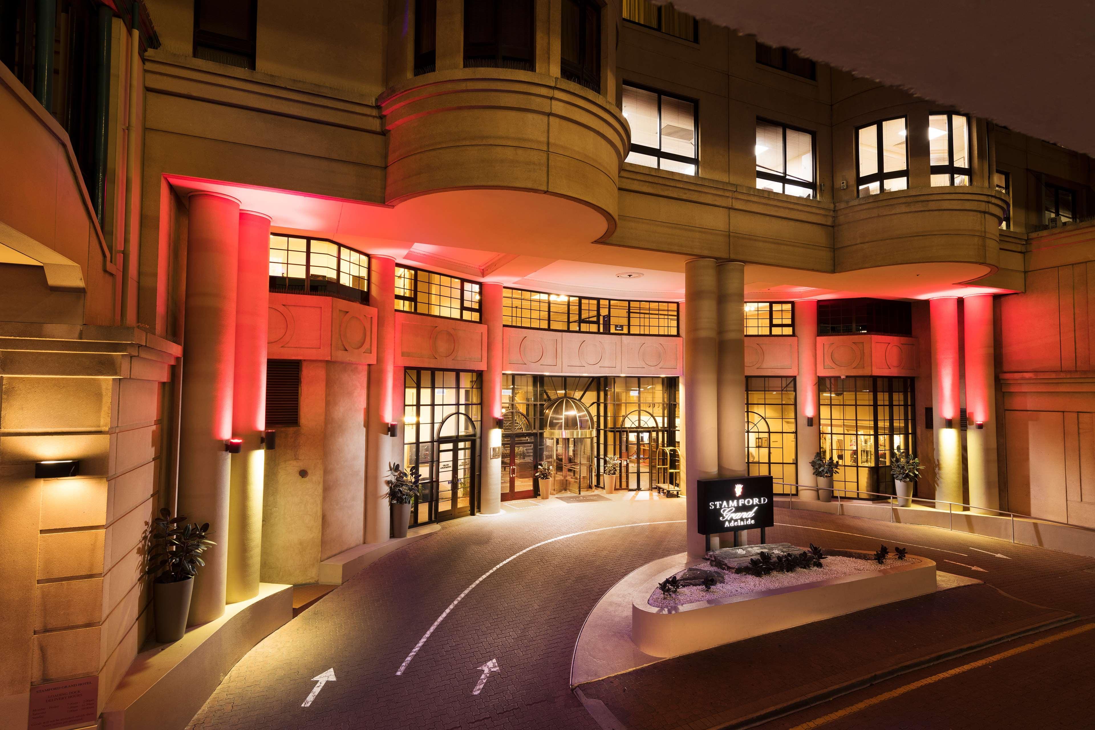 Stamford Grand Adelaide Hotel Glenelg Ngoại thất bức ảnh The photo shows the entrance of a hotel or luxury building at night. The façade features a modern architectural style with large windows and an elegant entrance. The area is illuminated with red lighting, creating an inviting atmosphere. There appear
