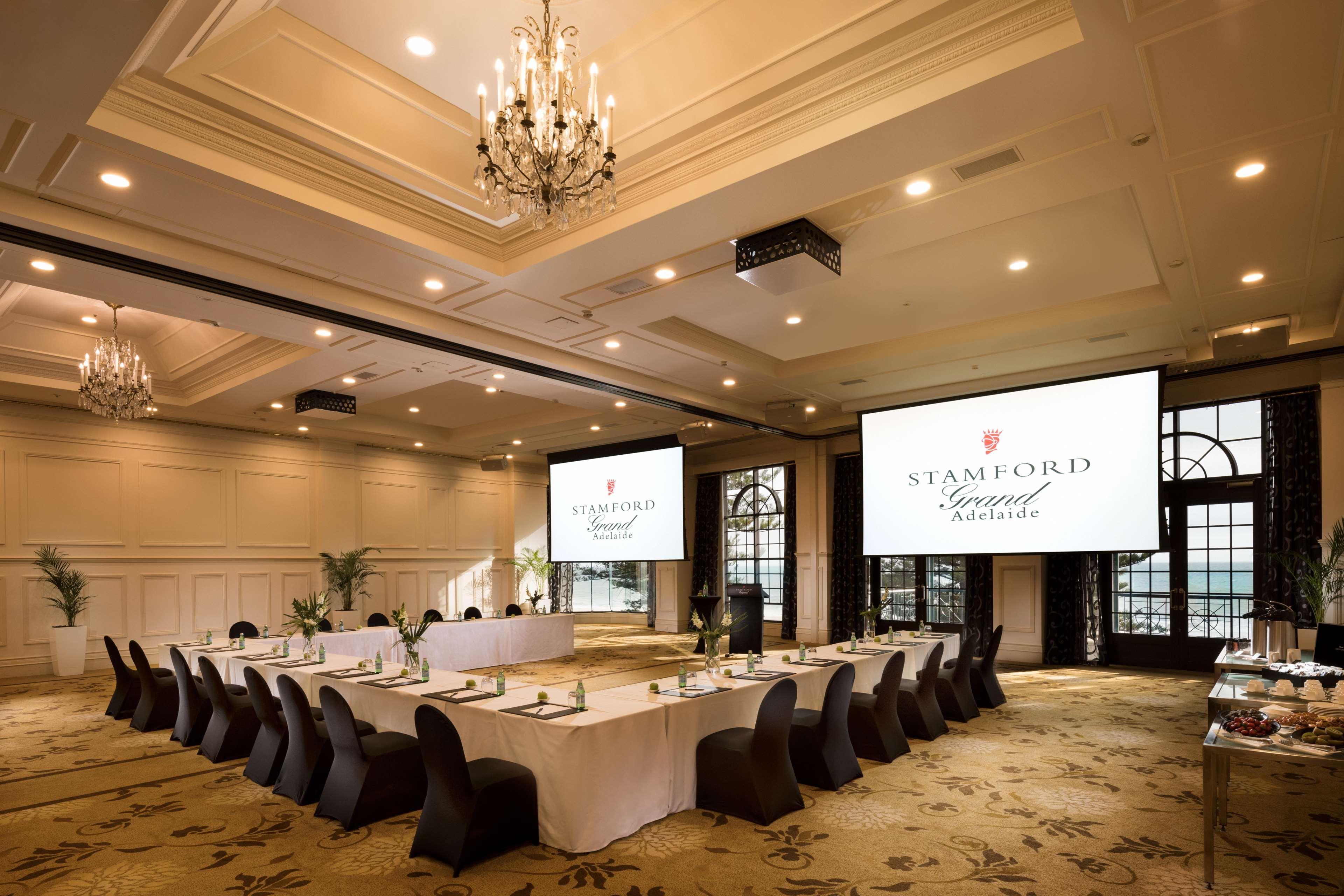 Stamford Grand Adelaide Hotel Glenelg Ngoại thất bức ảnh The photo shows a spacious and elegantly designed conference room. The room features a long table set for a meeting, surrounded by stylish chairs. Two large screens are positioned at the front, displaying the logo "Stamford Grand Melbourne." The ceil