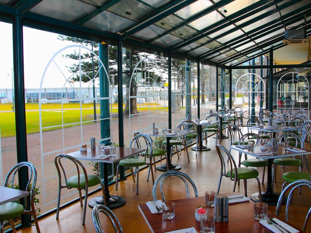 Stamford Grand Adelaide Hotel Glenelg Ngoại thất bức ảnh The photo shows the interior of a restaurant with a modern design. The space features several tables with green chairs, arranged in a way that allows for ample seating. Large glass windows provide a view of the outside, creating a bright and open atm