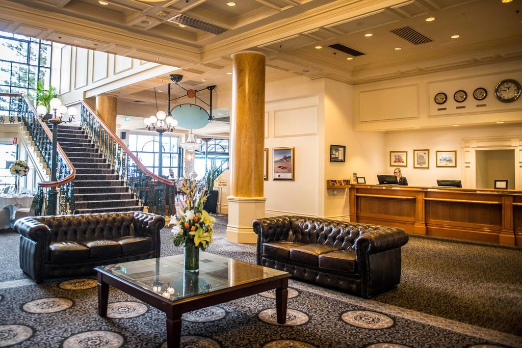 Stamford Grand Adelaide Hotel Glenelg Ngoại thất bức ảnh The photo depicts a hotel lobby featuring a spacious and elegant design. There are two dark leather sofas arranged in front of a glass coffee table, adorned with a floral centerpiece. The lobby has a refined atmosphere, highlighted by large windows t