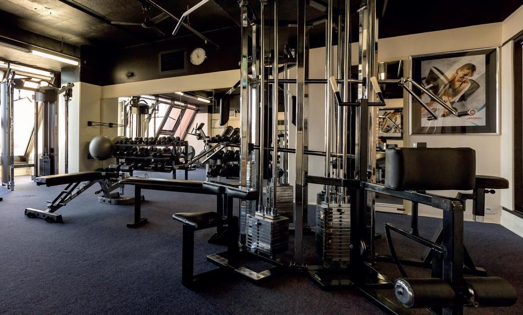 Stamford Grand Adelaide Hotel Glenelg Ngoại thất bức ảnh The photo shows a gym interior with several pieces of exercise equipment. In the foreground, there is a multi-station machine that features various pulleys and weights. To the side, there are benches and free weights, including dumbbells. The gym has